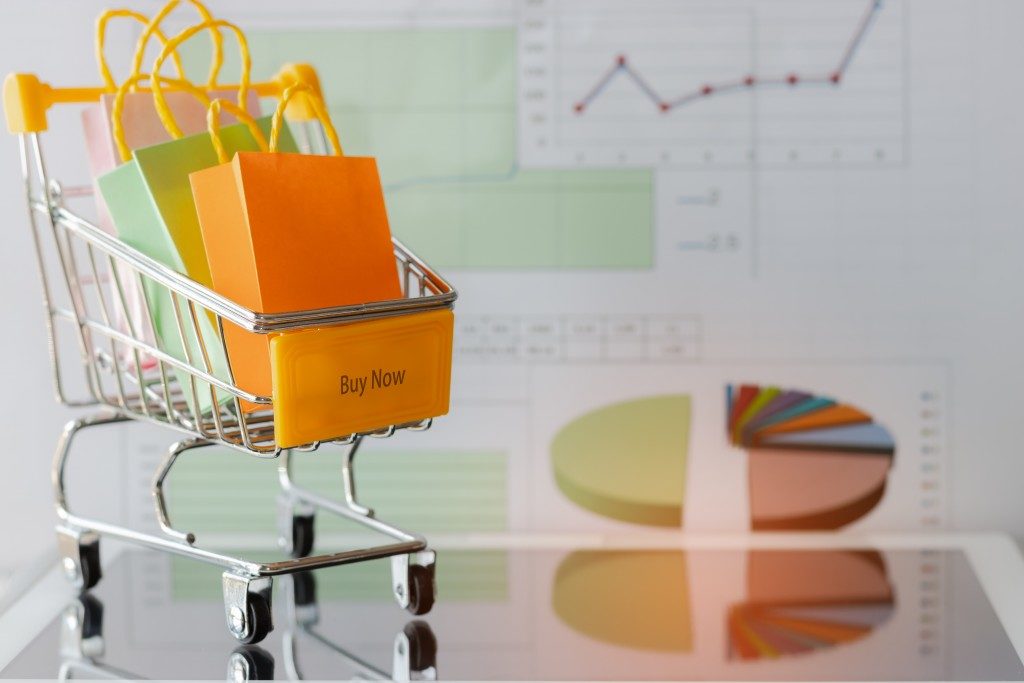Colourful paper bags in yellow trolley on tablet with chart background