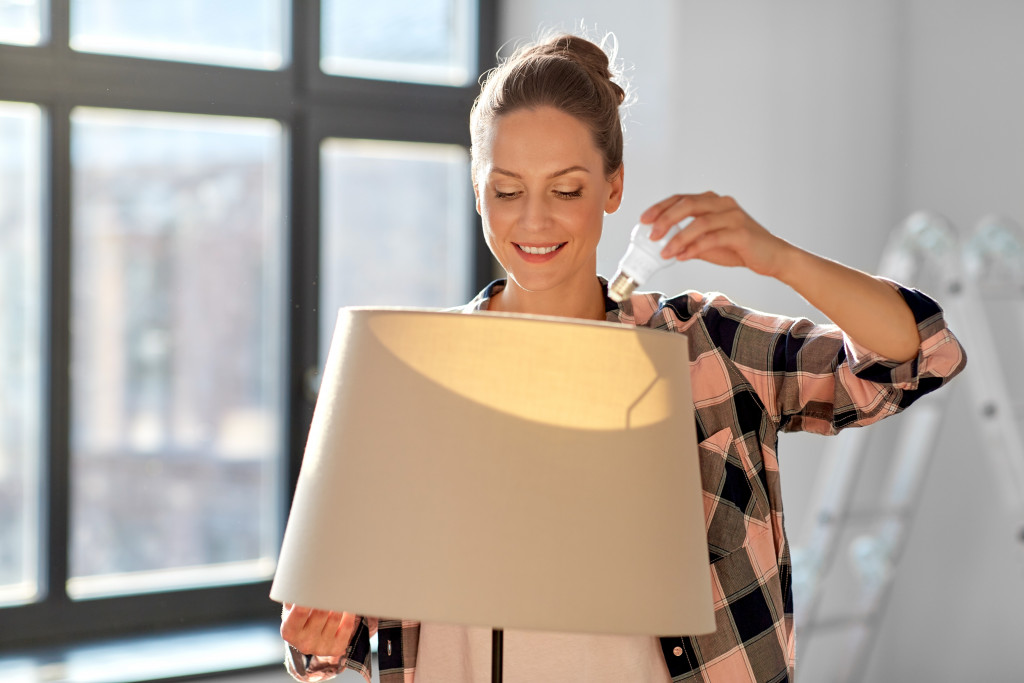 a woman holding a light bulb placing it on a lamp