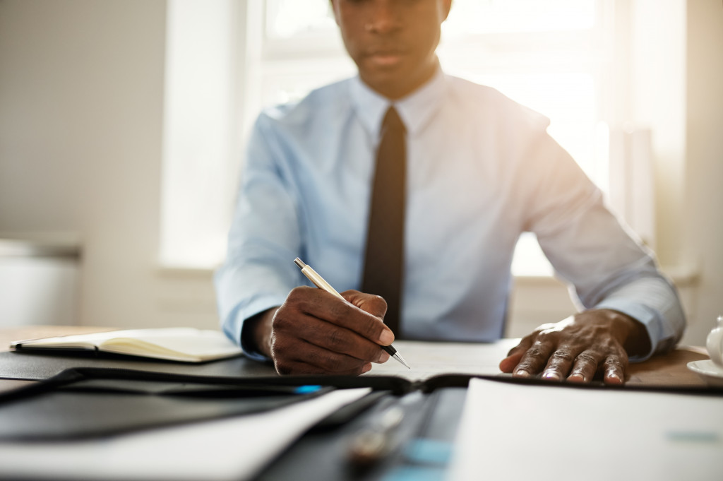 A man in his office writing, signing documents on his desk