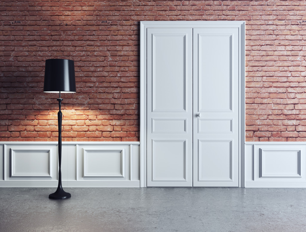 A floor lamp beside a door and a brick wall